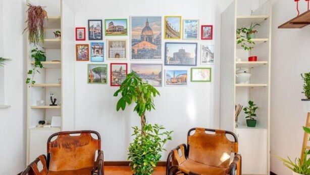 A room with two leather chairs, a central table with a woven placemat, and a wall adorned with framed pictures of various landmarks. - Cozy Apartment in the Heart of Rome- St. Peter's & Vatican (Roma)