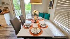 Een eetruimte met een tafel voor vier personen, een bloemenvaas en een raam met zonwering.