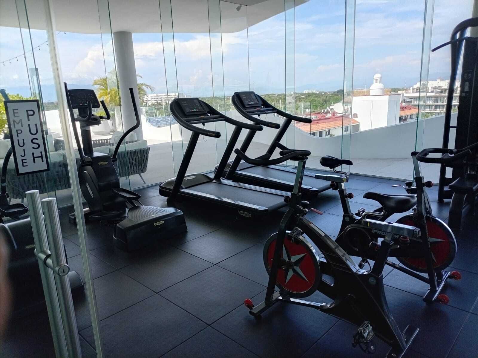 Een sportschool met fitnessapparatuur, een loopband en een hometrainer.