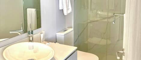 A modern bathroom with a glass-enclosed shower, a white sink, and a toilet.