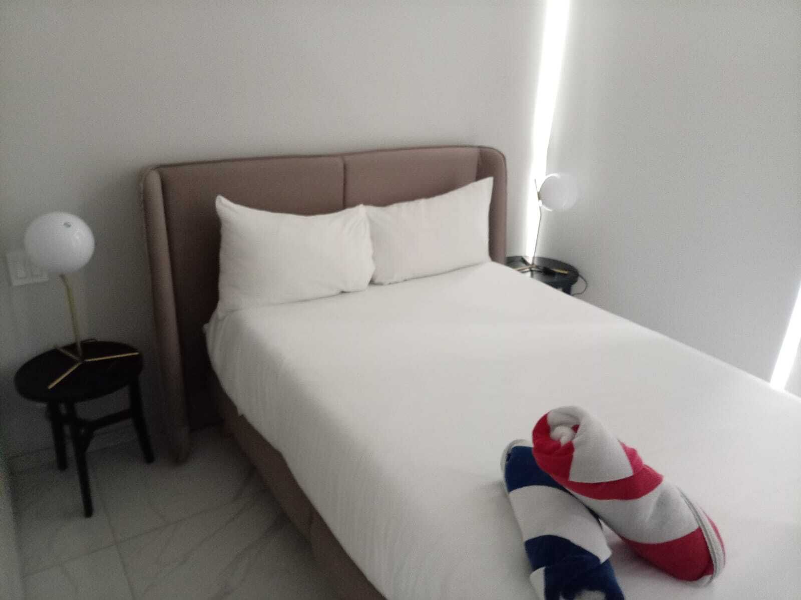 A hotel room with a bed, pillows, a bedside table, and a lamp.