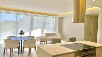 A modern kitchen with a central island, a dining area with a round table and chairs, and a large window providing a view of the city.