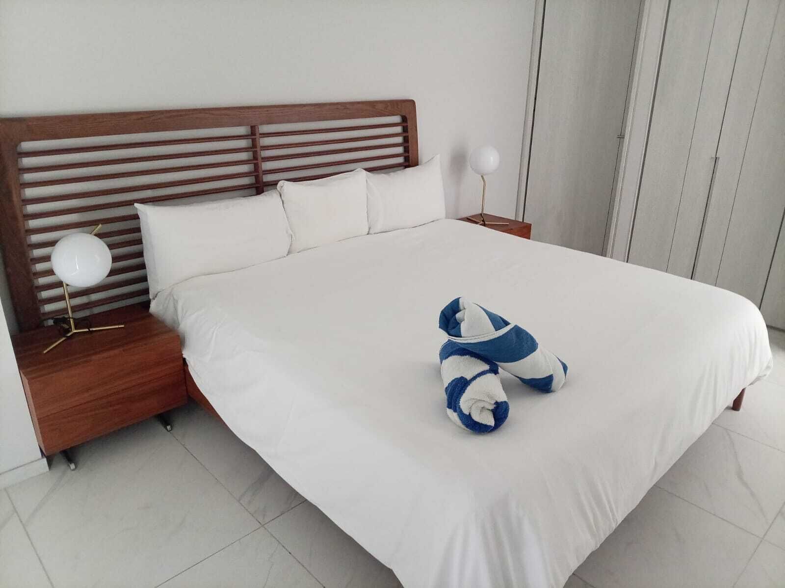 A neatly made bed with white bedding and a blue and white pillow.