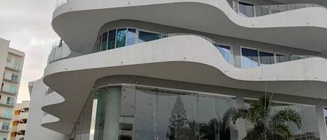 A modern multi-story building with a unique wavy architectural design, featuring large glass windows and a central entrance with steps.