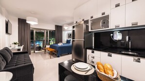 A modern hotel room with a living area, a dining table with a basket of bread, a kitchen with a refrigerator and microwave, and a large window with curtains. - 112 Rosemari's Apartments Studio Premium Centro SP Garage & Pool & Gym (República São Paulo)
