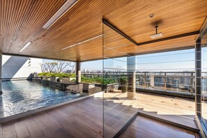 A modern indoor pool with wooden flooring and glass walls, offering a view of the city skyline.