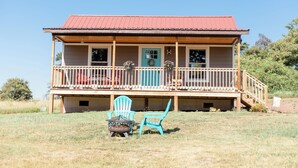 Une maison à deux étages avec un toit rouge, une véranda dotée de balustrades en bois et une porte bleue.