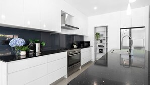 A modern kitchen with white cabinetry, a black countertop, stainless steel appliances, and a black speckled floor. - Marine Adventures – tranquil blue waters and white beaches of Jervis Bay (Callala Bay)