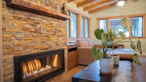 Un salon chaleureux avec une cheminée en pierre, des poutres apparentes en bois au plafond et une grande fenêtre.