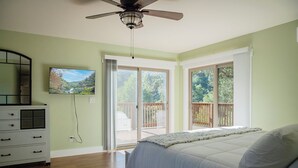 Une chambre avec un lit, une commode, un ventilateur de plafond et un téléviseur fixé au mur.