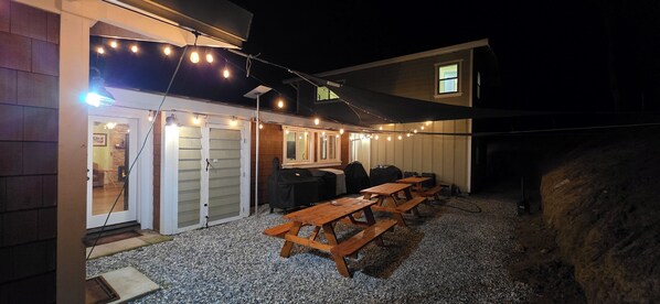 An outdoor patio with wooden picnic tables and string lights.