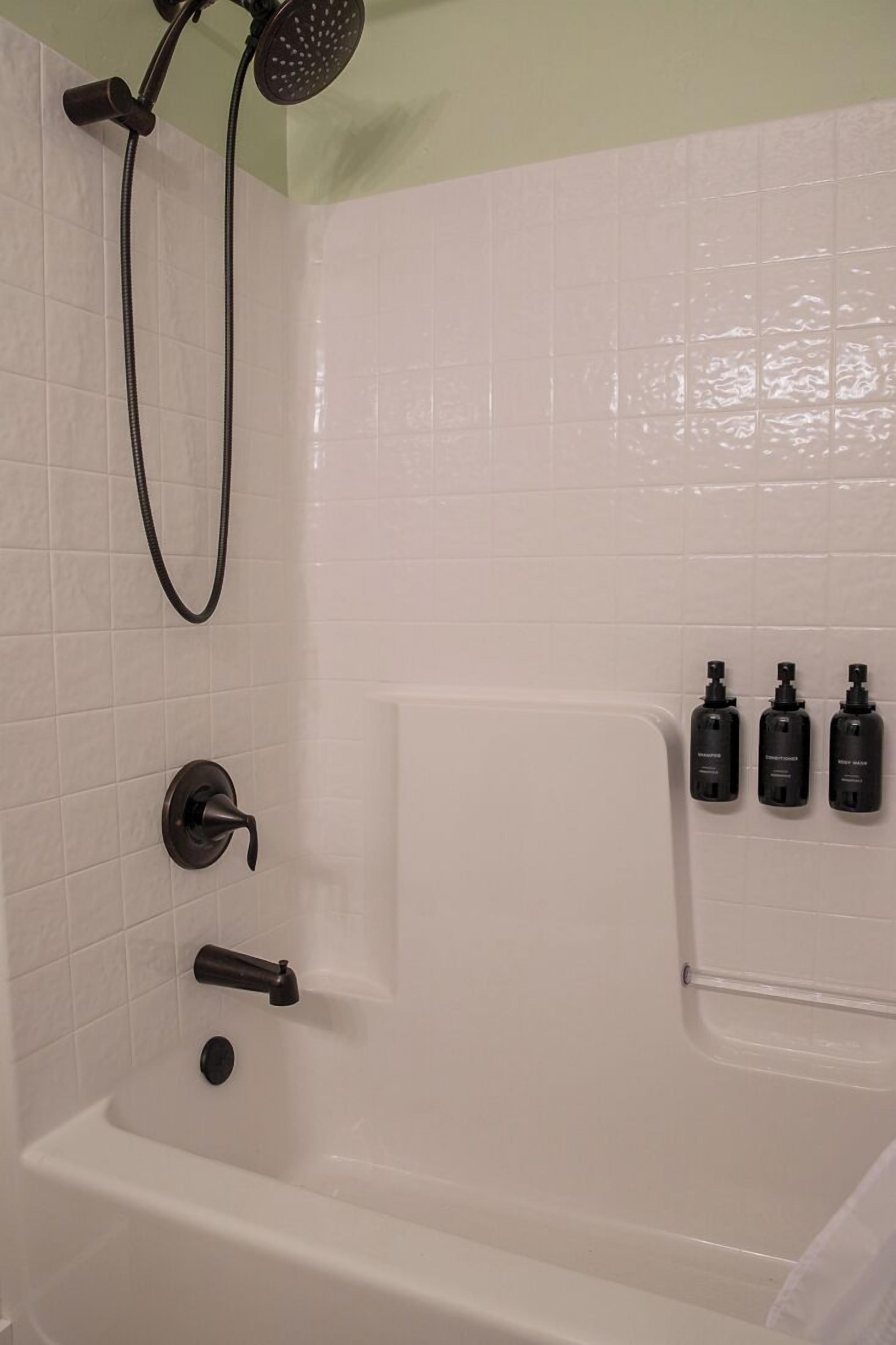 A bathroom with a bathtub, a showerhead, and three bottles of shampoo on the wall.