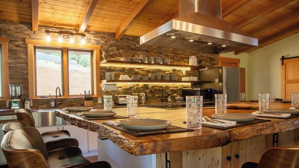 Une cuisine moderne avec un mur de crédence en pierre, des poutres en bois au plafond et un îlot central doté de sièges de bar.