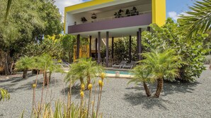 A modern building with a yellow and purple facade, a pool, and surrounding tropical plants. - Unique architectural villa with private pool on nature resort (Sint Michiel)