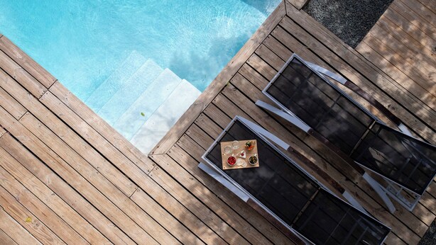 A wooden deck with a pool, a table with a glass of water, and a chair. - Unique architectural villa with private pool on nature resort (Sint Michiel)