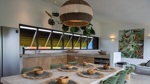 A modern kitchen with a large island, green chairs, and a dining table set with wooden bowls. - Unique architectural villa with private pool on nature resort (Sint Michiel)