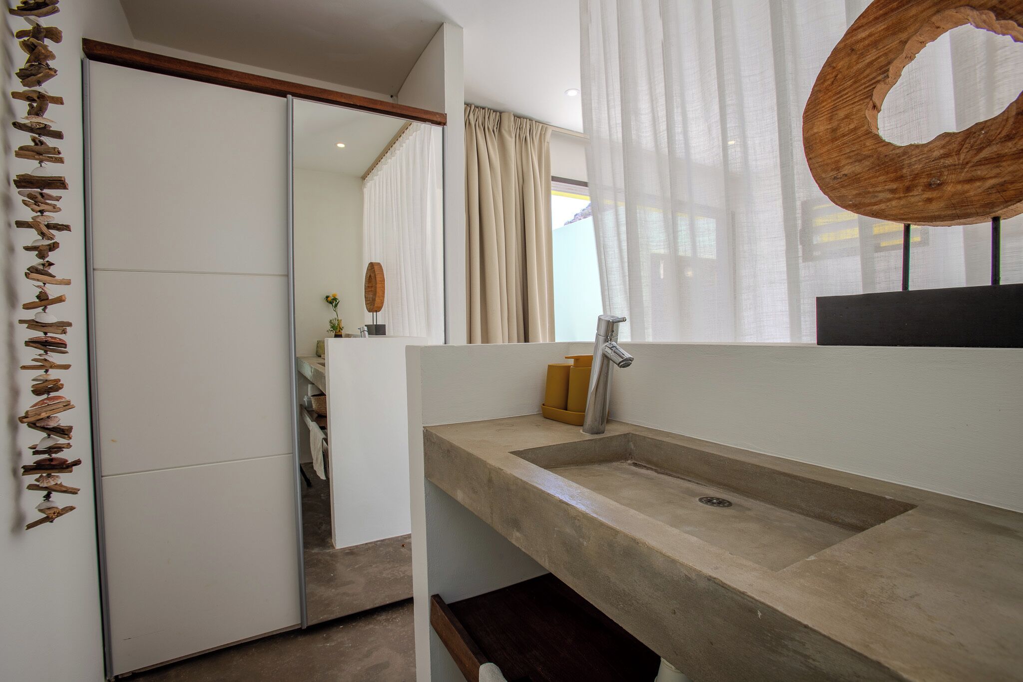 A modern bathroom with a large mirror, a beige sink, and a wooden decorative piece above the mirror.