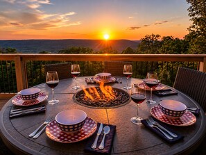 A round outdoor dining table with chairs, surrounded by a fire pit, set against a sunset view. - A-Frame Cabin (Independence) - by Red White and Blue Views (Lookout Mountain)