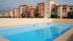 A swimming pool with a clear blue water surface, surrounded by a low white wall. - Superb modern 2/4-person apartment with swimming pool (Le Barcarès)