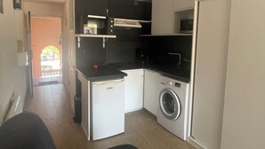 A compact kitchen with a washing machine, a microwave, and a small refrigerator. - Superb modern 2/4-person apartment with swimming pool (Le Barcarès)