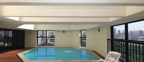 A rooftop pool with a wooden deck and a white lounge chair.