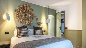 Ein ordentlich bezogenes Bett mit einer karierten Tagesdecke, ein an der Wand befestigtes abstraktes Kunstwerk und zwei Pendelleuchten.