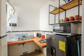 A compact kitchen with a gas stove, a microwave, a refrigerator, a sink, and a shelf with decorative items. - Edificio Aurora (Mexico City)