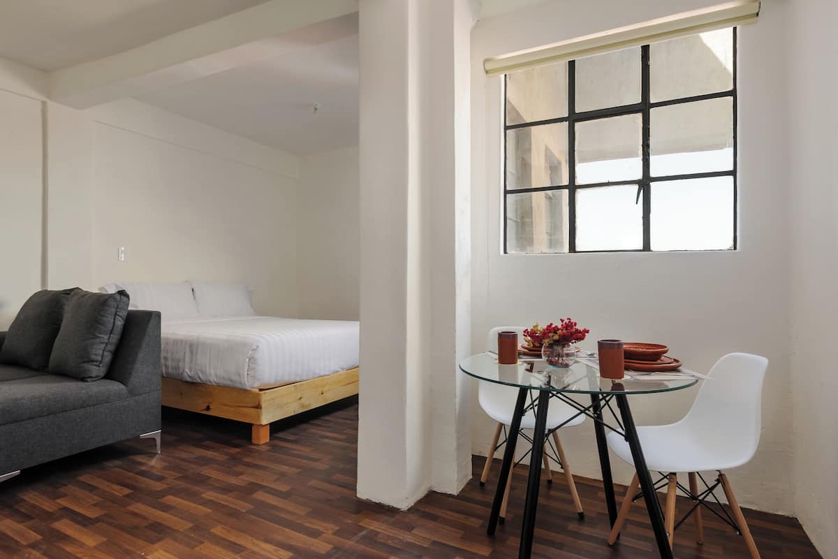 A bedroom with a bed, a sofa, a glass table with chairs, and a window.