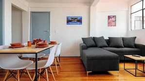 Una sala de estar moderna con un sofá seccional gris, una mesa de comedor de madera con sillas blancas y una pequeña mesa de centro.