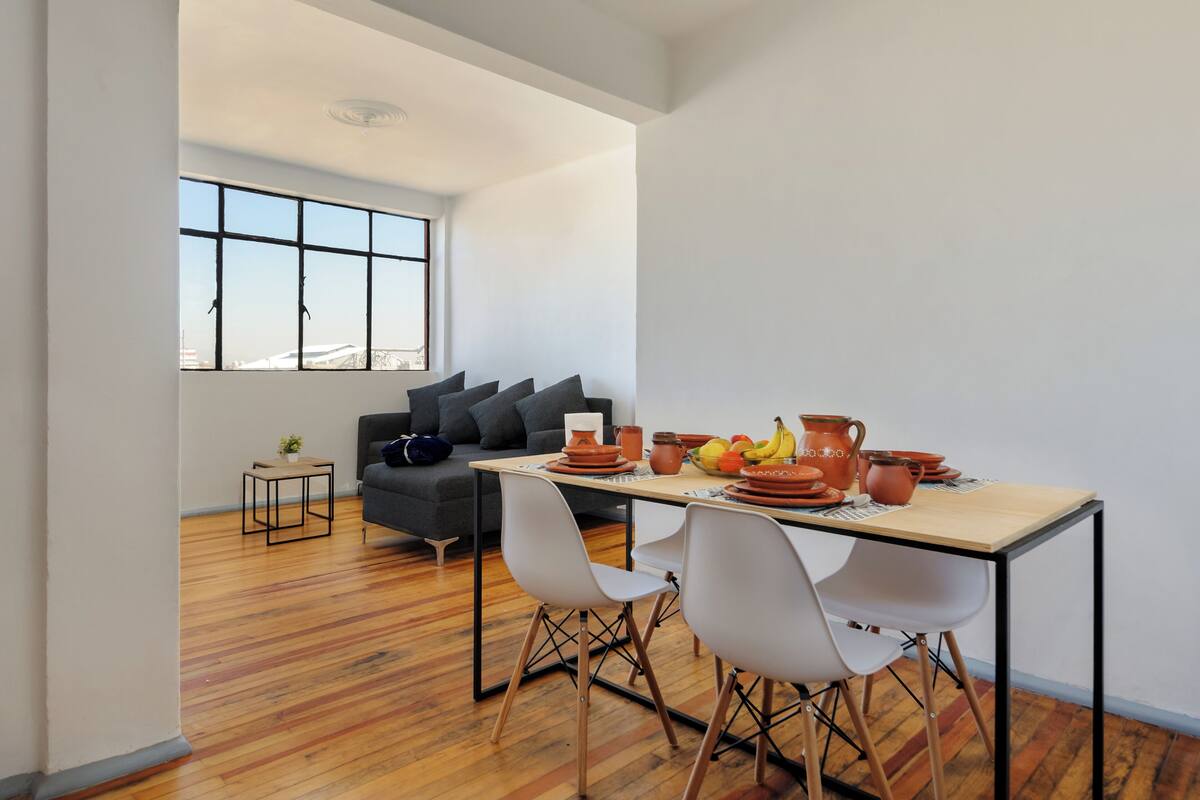 A modern living room with a sofa, dining table, chairs, and a large window.
