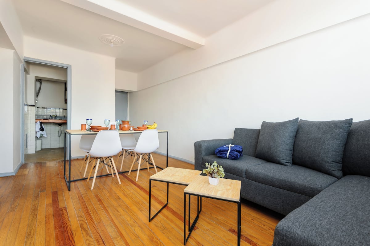 A modern living room with a grey sofa, wooden flooring, and a small table with a plant.