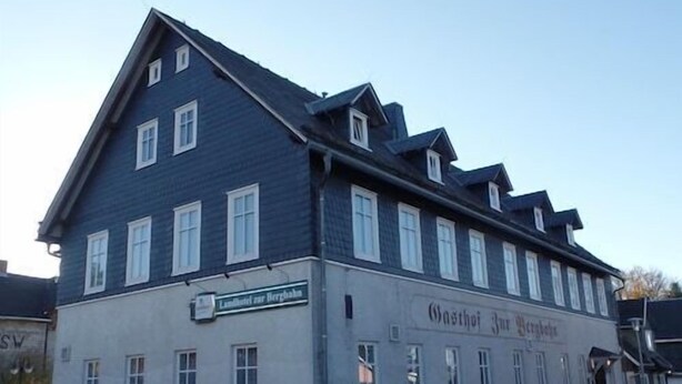 En tvåvåningsbyggnad med en mörkblå fasad och vita detaljer. Byggnaden har flera fönster och en skylt med texten ”Hotel zur Burg”.