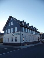 A two-story building with a dark blue facade and white trim. The building has multiple windows and a sign that reads "Hotel zur Burg".