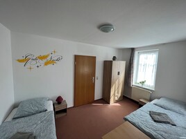Quarto com duas camas, um guarda-roupa, um radiador e uma janela com cortinas.