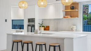 Una cocina moderna con armarios blancos, una isla grande con taburetes, microondas, horno y una lámpara colgante.