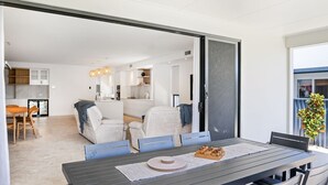 Un comedor moderno con una mesa dispuesta para cuatro, una cocina al fondo y un gran ventanal corredizo que da a un balcón con una planta.