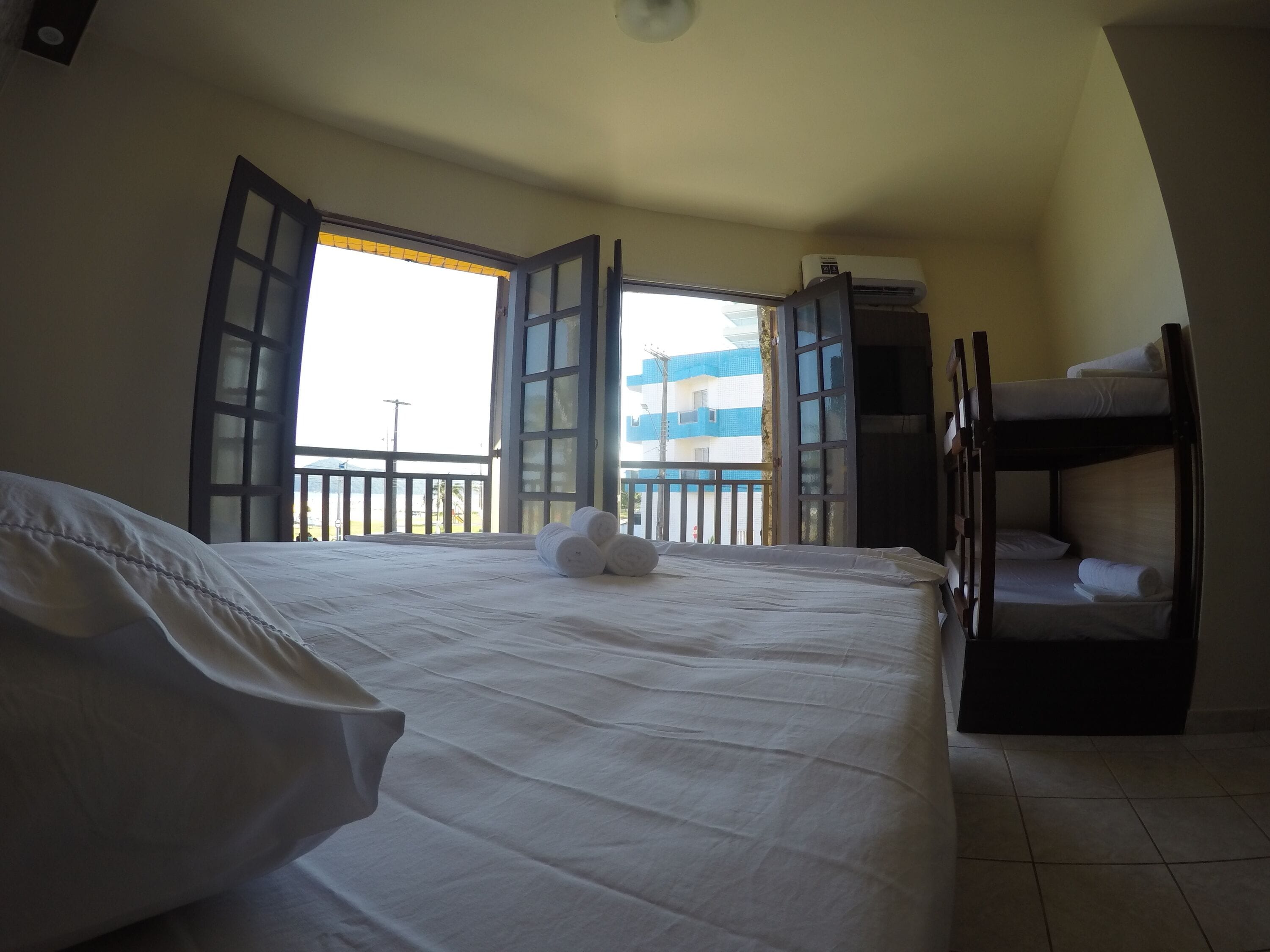 Quarto de hotel com uma cama grande, uma cama beliche e uma varanda com portas abertas.