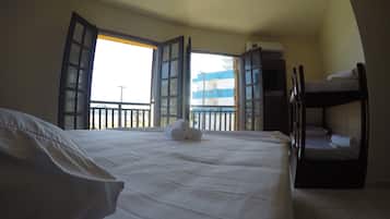 Quarto de hotel com uma cama grande, uma cama beliche e uma varanda com portas abertas.
