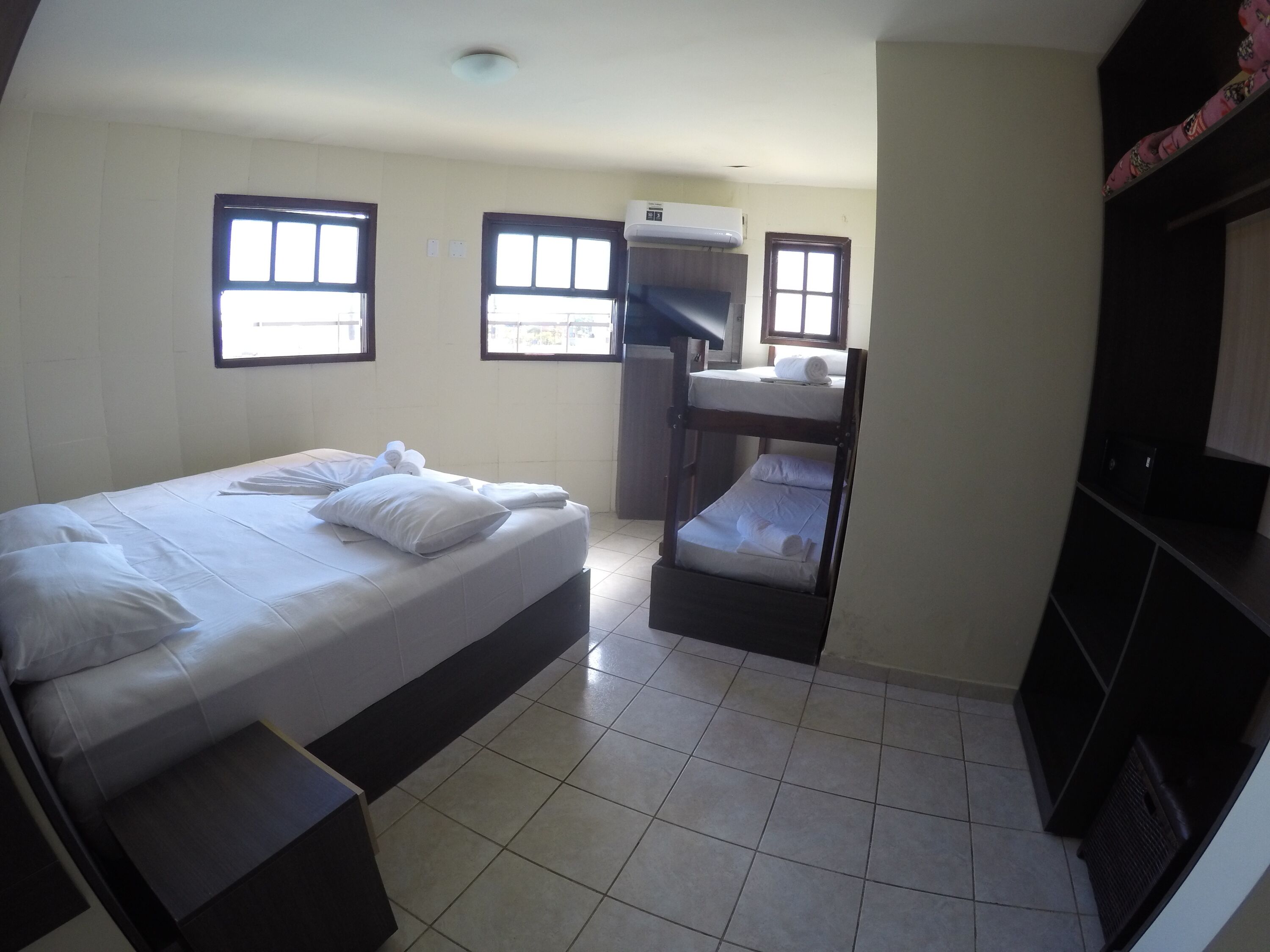 A compact hotel room with a bunk bed, a small desk with a chair, a window, and an air conditioning unit.