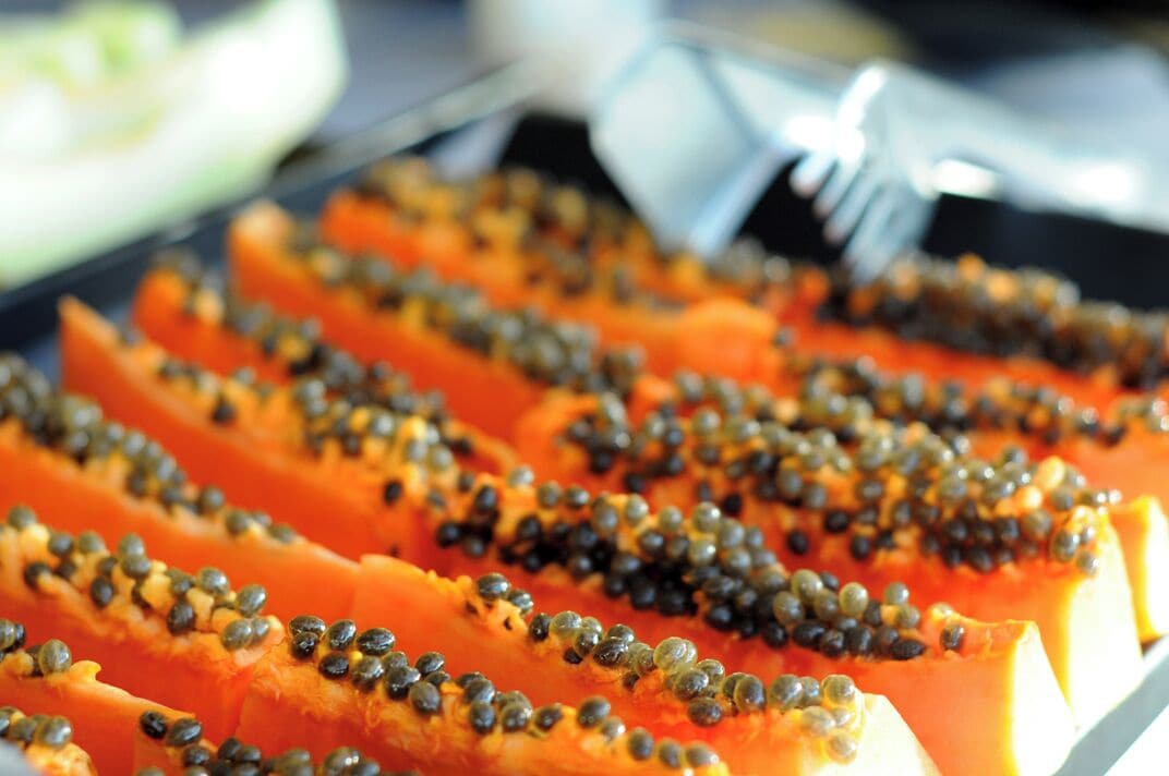 A close-up of sliced papaya topped with black seeds.