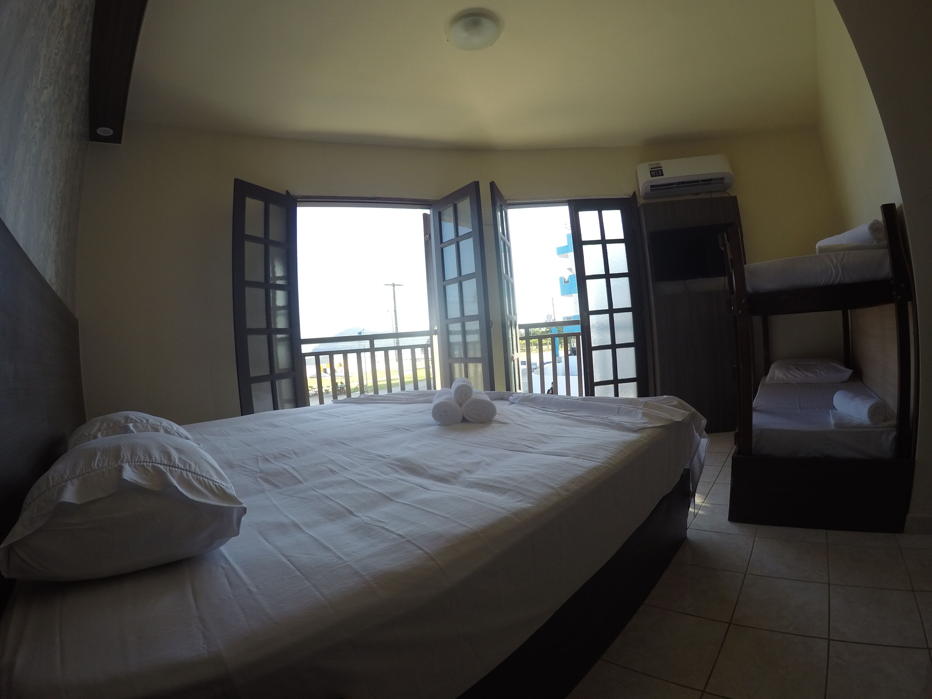 A hotel room with a bed, a window, an air conditioning unit, and a bunk bed.