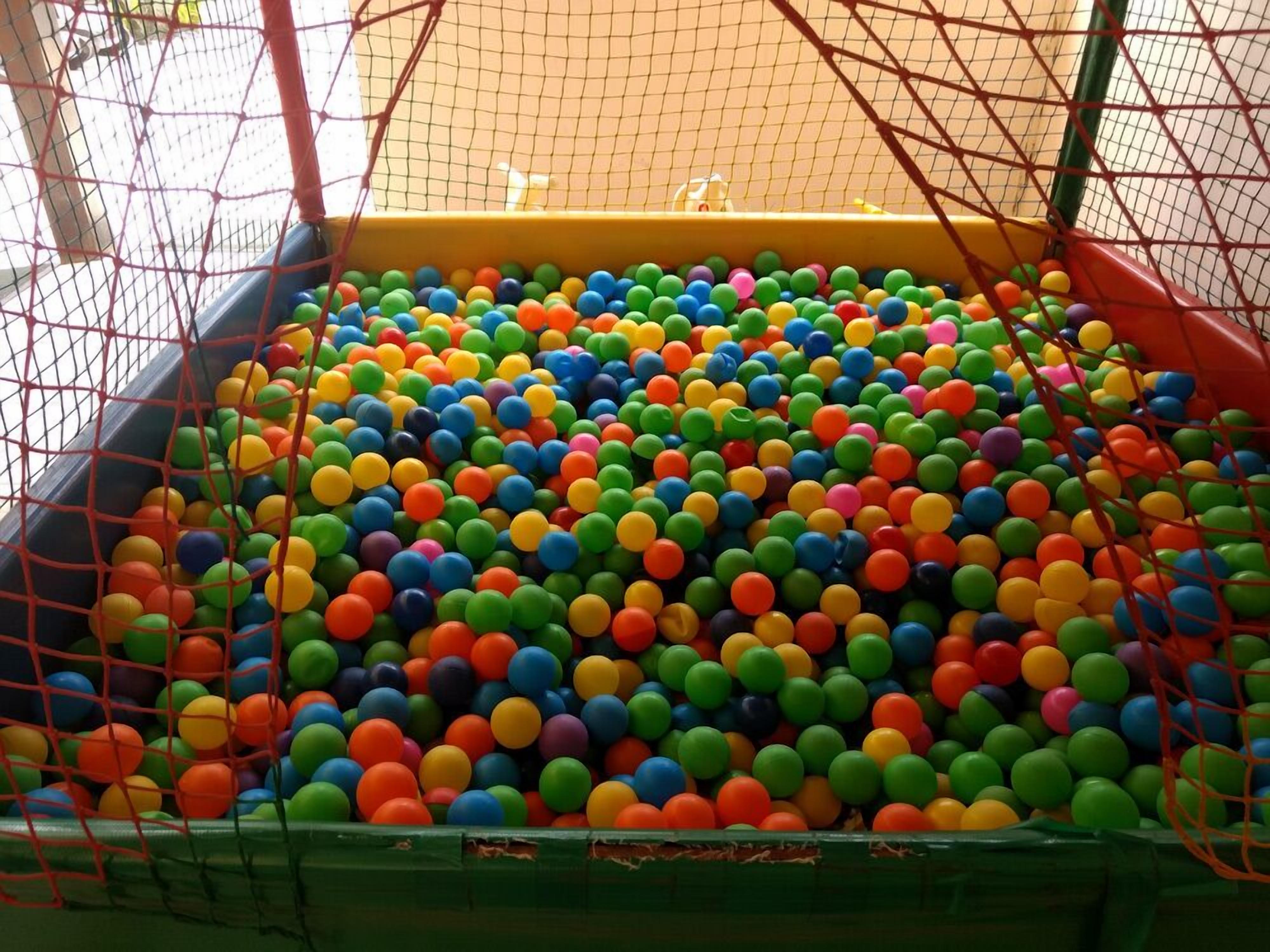 A ball pit filled with multicolored plastic balls, surrounded by a safety net.