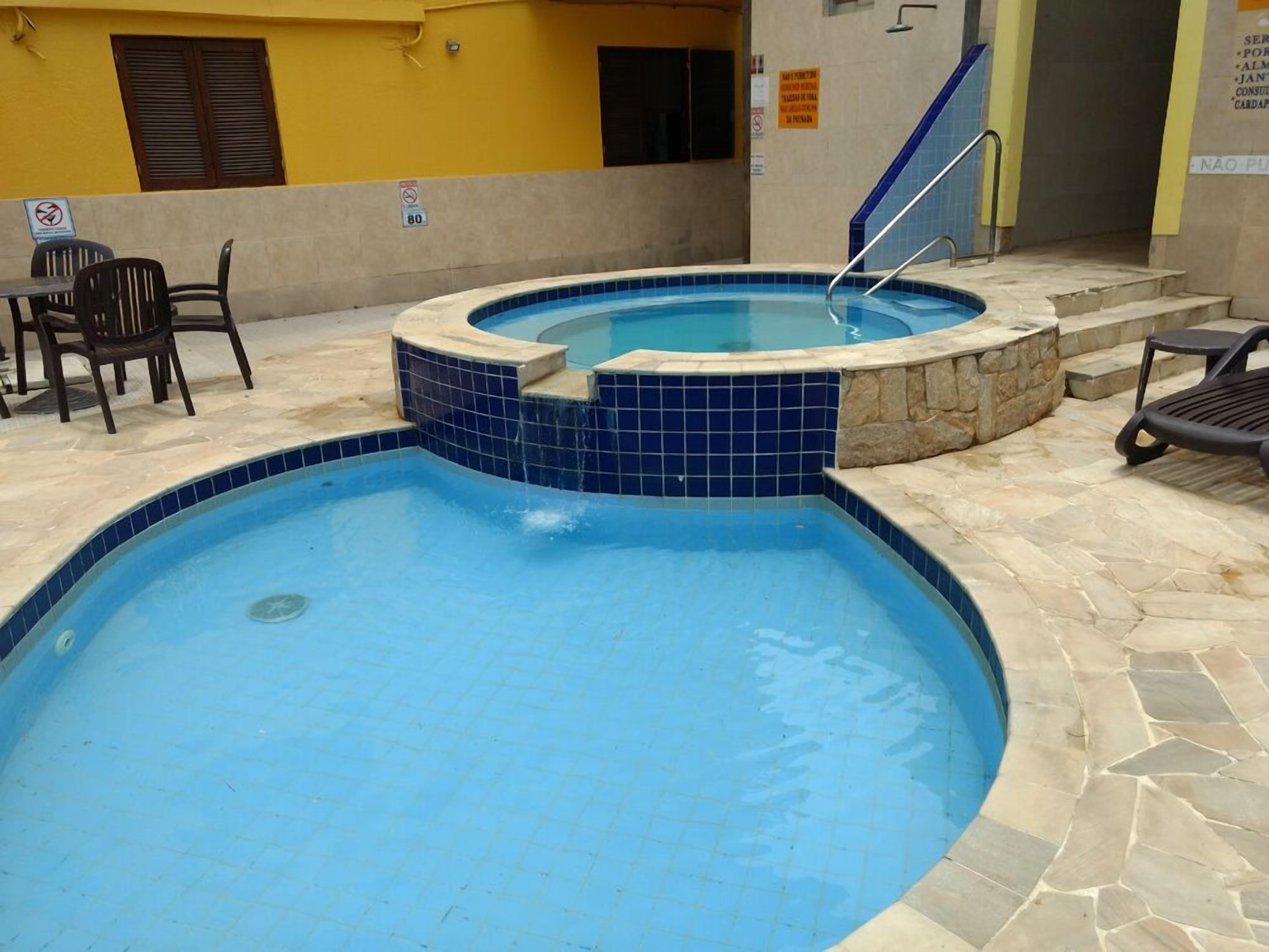 Una piscina con borde de piedra y azulejos, un pequeño jacuzzi y algunas sillas.