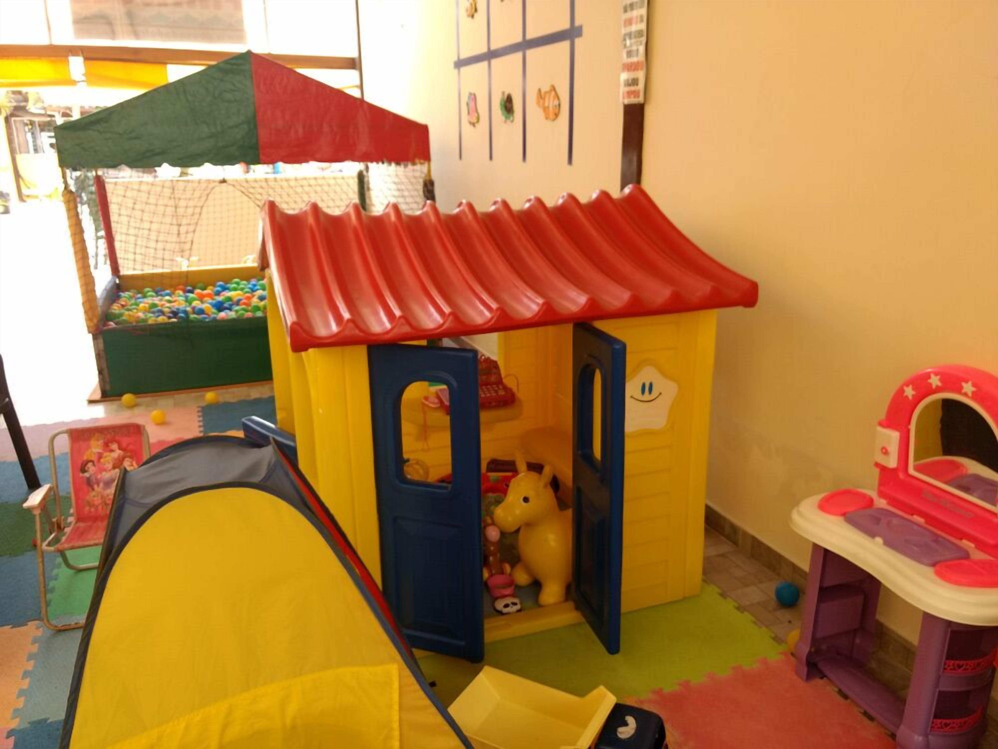 Zona de juegos con una casita amarilla, techo rojo y piscina de pelotas.