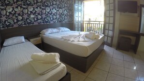 A hotel room with two beds, a large floral-patterned wall, a balcony with a view, and a TV mounted on the wall. - Pousada do Francês (Bertioga)