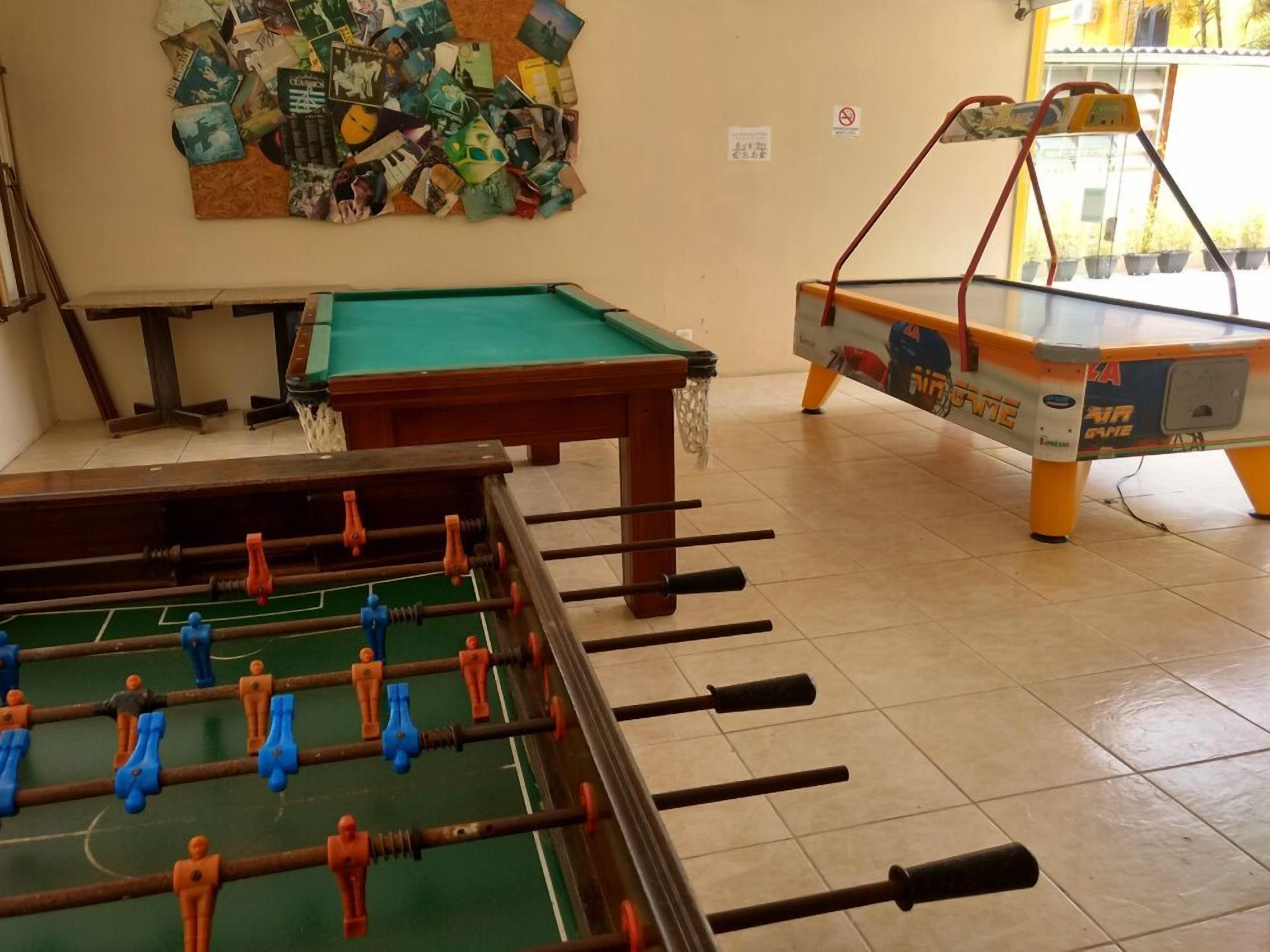 Una mesa de billar, una mesa de fútbol de mesa y una mesa de carambola en una sala con suelo de baldosas y una pared decorada con diversos objetos.