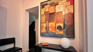 Une pièce avec un sol à carreaux noirs et blancs, une chaise noire, une console noire sur laquelle repose un objet sphérique blanc, et un grand tableau abstrait accroché au mur.