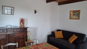 A room with a wooden dining table, a dark sofa, a wooden cabinet, and a painting on the wall. - Gite du Fourbas - renovated in 2025 - with swimming pool (Belmont-Sainte-Foi)