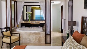 Een slaapkamer met een groot bad, een stoel, een bed en uitzicht op de oceaan.