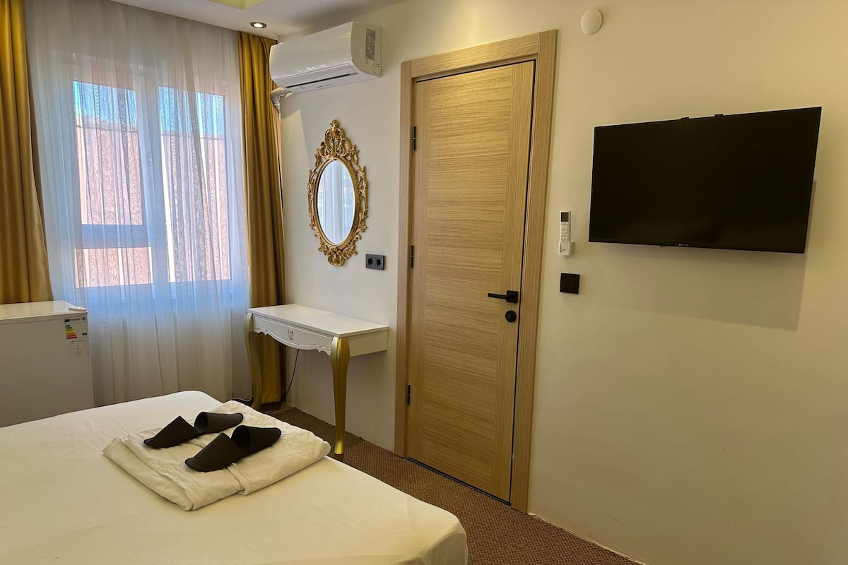 A hotel room with a bed, a vanity with a mirror, a television, and a door.